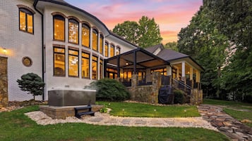 A modern house with a stone exterior, large windows, a covered patio, and a hot tub.