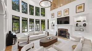 A spacious living room with a fireplace, large windows, and a modern sofa set. - Lion Manor by Avantstay Spacious Lake Norman Home Hot Tub + Tennis Court + Firepit + Deck (Denver)