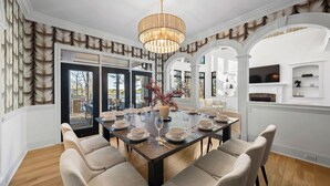 Un coin repas avec une grande table dressée pour six personnes, entourée de chaises, et un lustre au-dessus.