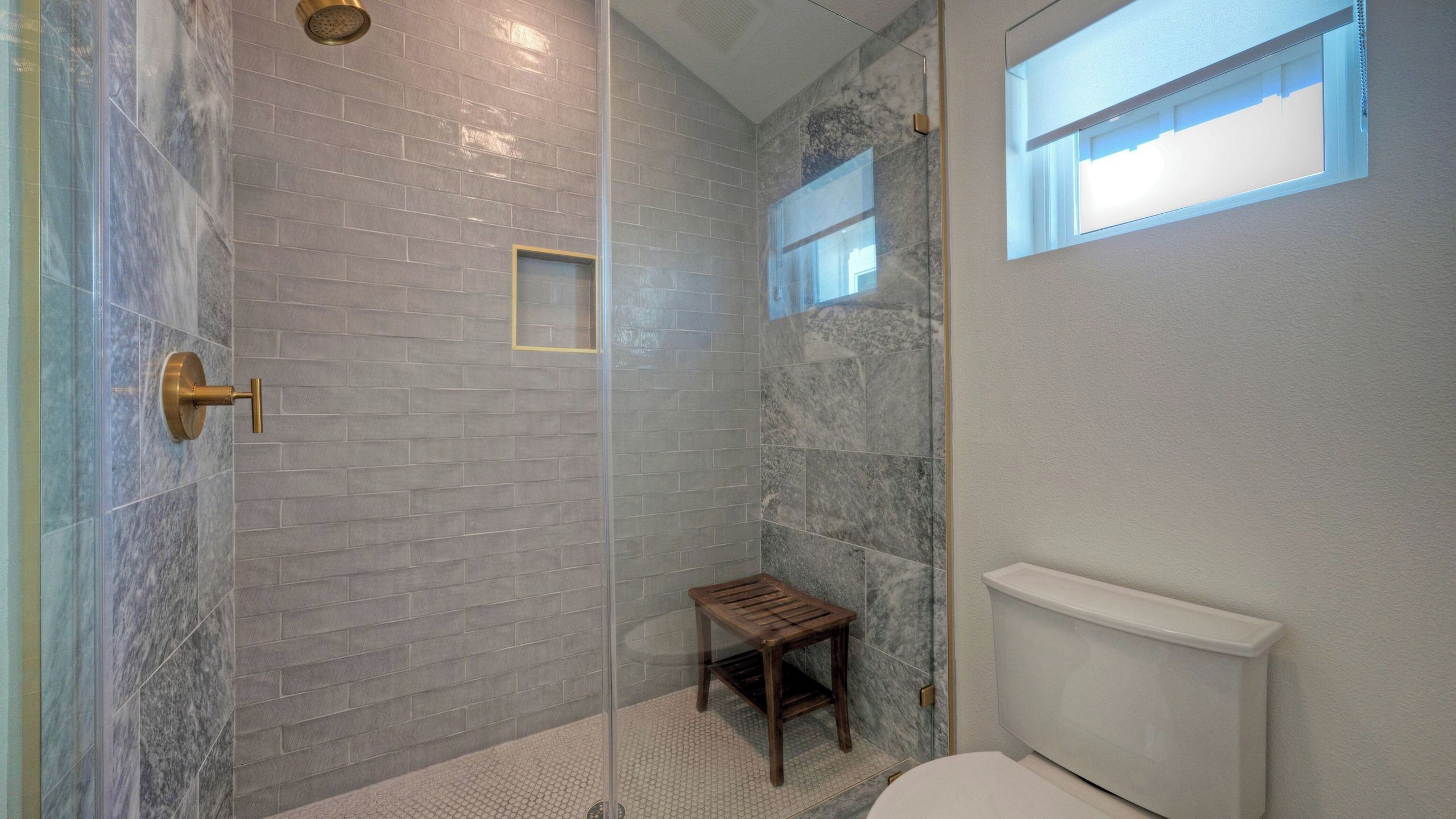 A bathroom with a glass shower enclosure, a wooden stool, and a toilet.