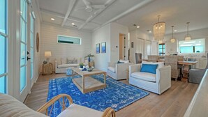 Ein geräumiges Wohnzimmer mit hohen Decken, eine Essecke mit Rattanmöbeln und eine Küche mit großen Fenstern.