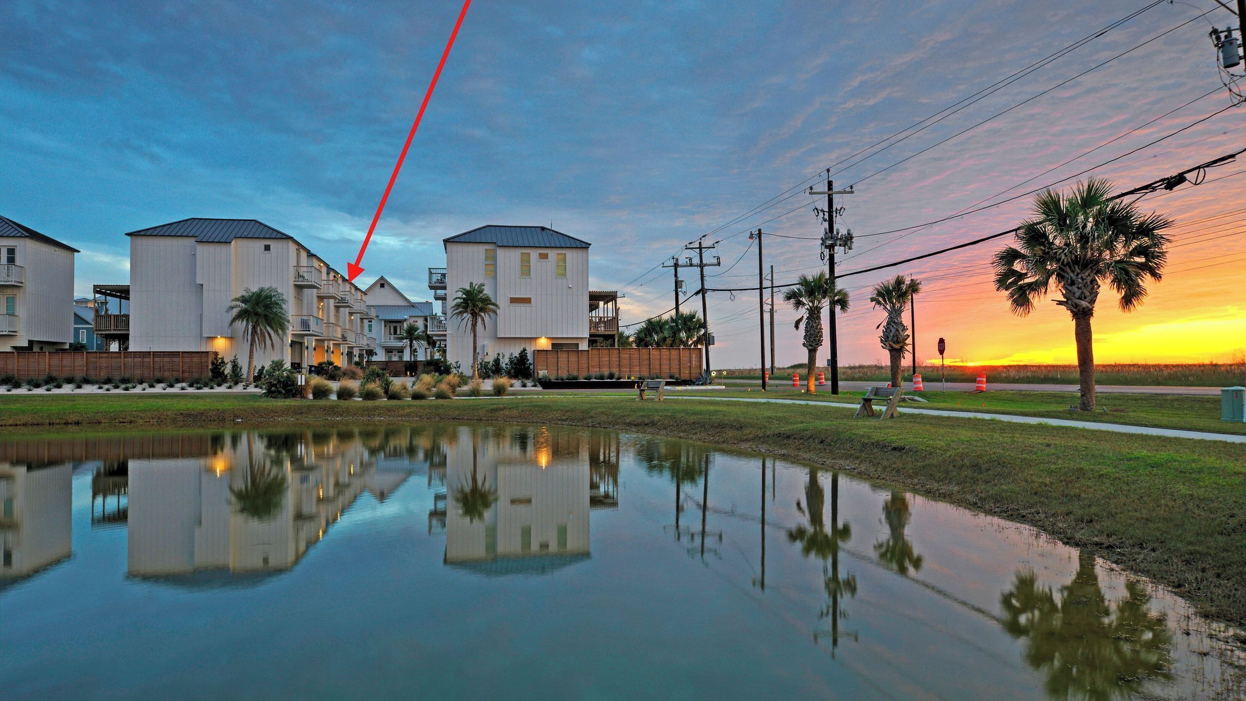 A waterfront residential area with modern buildings, a calm water body reflecting the structures, and a sunset in the background.