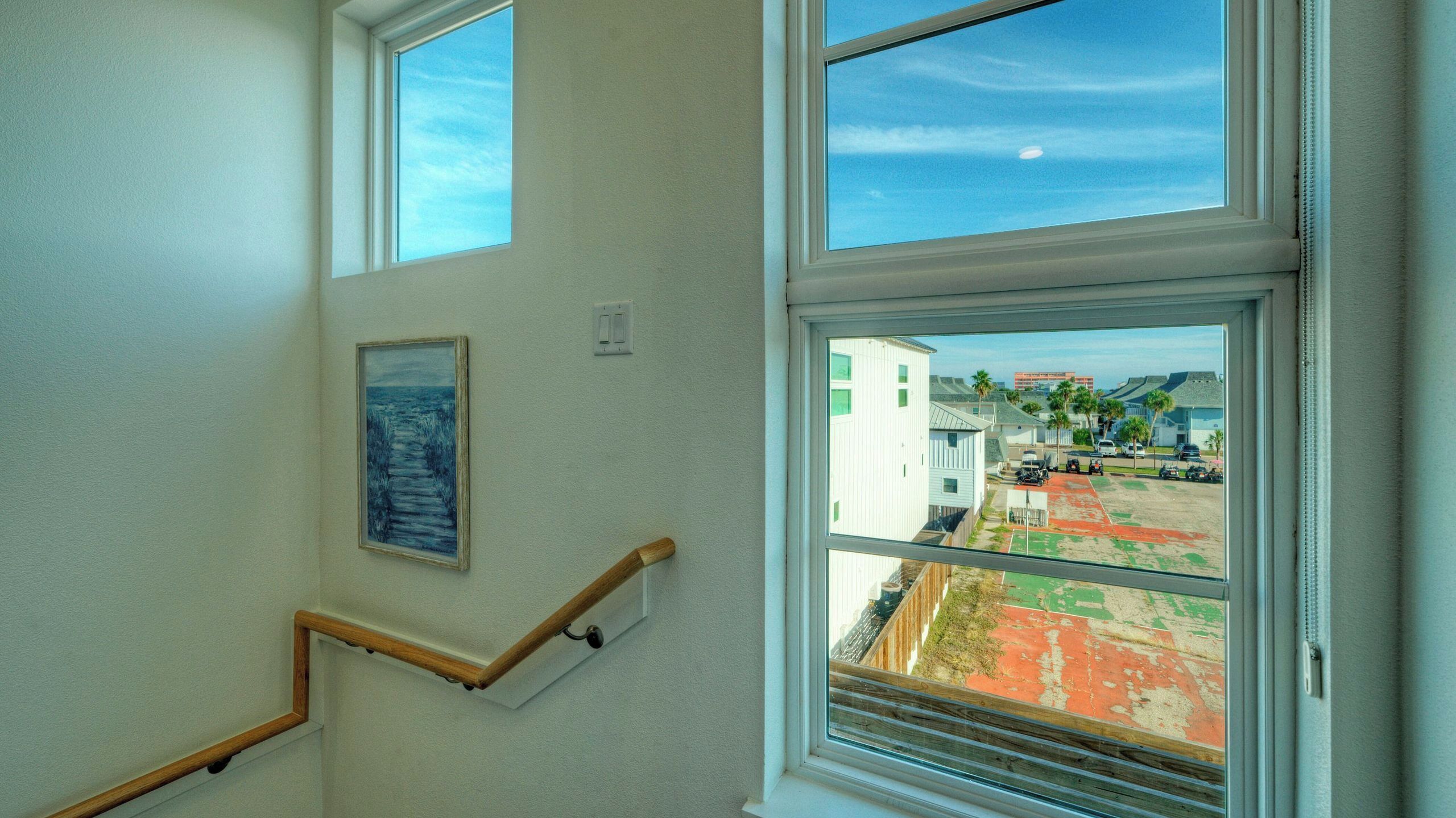 A staircase with a handrail, a framed picture on the wall, and a view of a parking lot through a window.