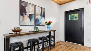 A modern bar area with abstract art, a vase with flowers, and a black door with a view of greenery. - Modern Smoky Mountain Retreat w/ Hot Tub, Game Room & Movie Theater Heavens View by Avantstay (Pigeon Forge)