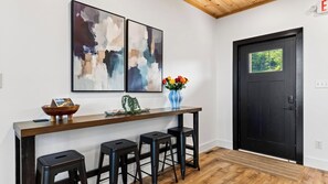 A modern bar area with abstract art, a vase with flowers, and a black door with a view of greenery. - Modern Smoky Mountain Retreat w/ Hot Tub, Game Room & Movie Theater Heavens View by Avantstay (Pigeon Forge)