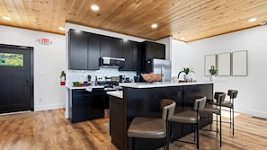 A modern kitchen with dark cabinets, stainless steel appliances, and a bar area with stools. - Modern Smoky Mountain Retreat w/ Hot Tub, Game Room & Movie Theater Heavens View by Avantstay (Pigeon Forge)