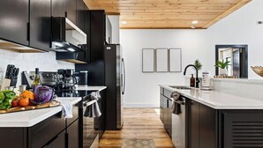 A modern kitchen with dark cabinetry, a stainless steel refrigerator, and a wooden ceiling. - Modern Smoky Mountain Retreat w/ Hot Tub, Game Room & Movie Theater Heavens View by Avantstay (Pigeon Forge)