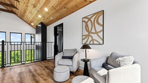 A modern living room with a wooden ceiling, a large abstract painting, and a balcony with a view. - Modern Smoky Mountain Retreat w/ Hot Tub, Game Room & Movie Theater Heavens View by Avantstay (Pigeon Forge)