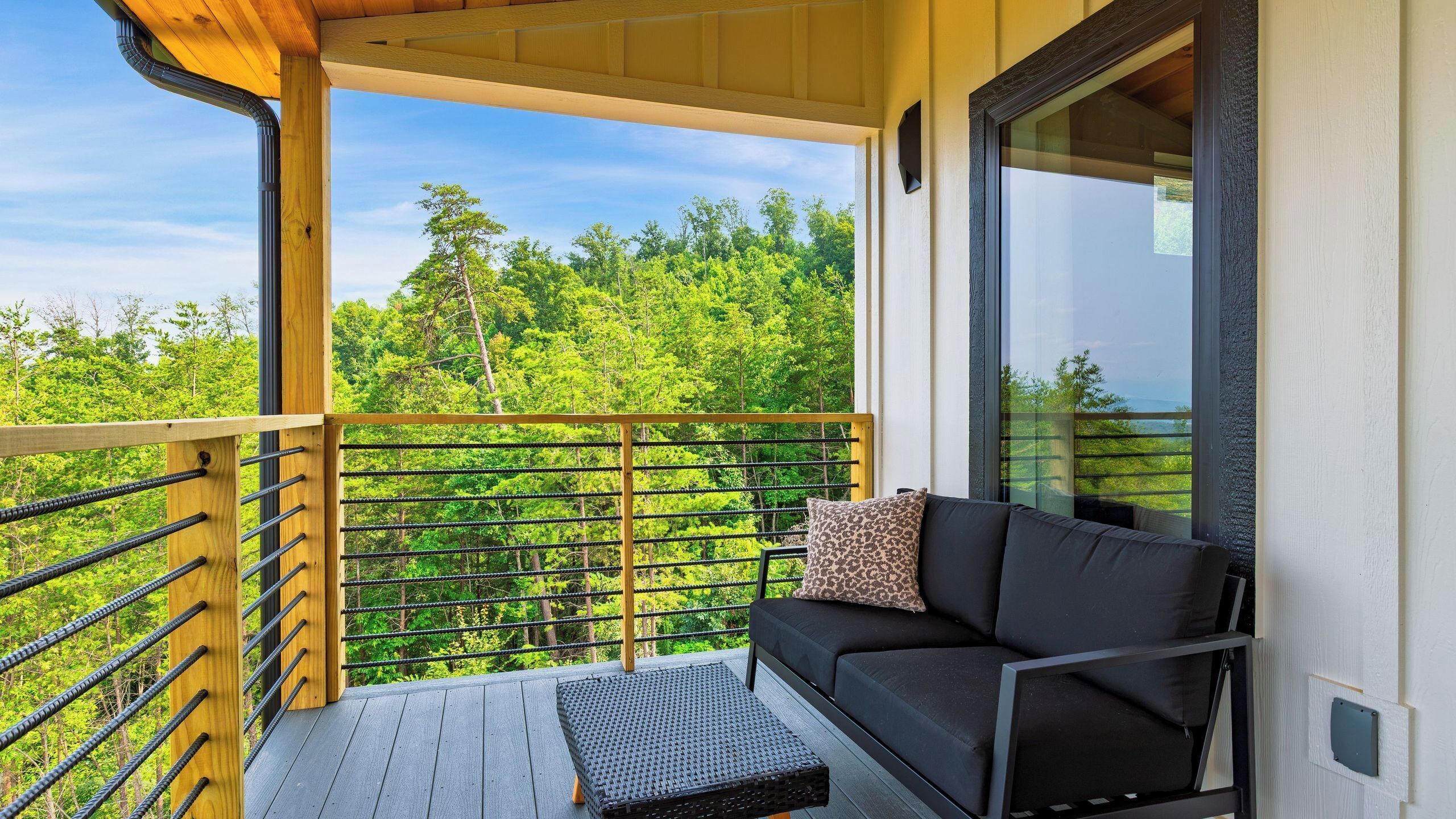 A balcony with a sofa and a small table, overlooking a forested area.