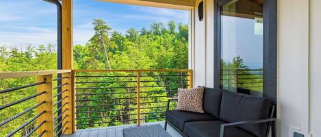 A balcony with a sofa and a small table, overlooking a forested area.