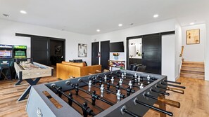 A room with a foosball table, a sofa, a TV, and a bookshelf. - Modern Smoky Mountain Retreat w/ Hot Tub, Game Room & Movie Theater Heavens View by Avantstay (Pigeon Forge)