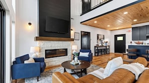 A modern living room with a fireplace, seating, and a kitchen area. - Modern Smoky Mountain Retreat w/ Hot Tub, Game Room & Movie Theater Heavens View by Avantstay (Pigeon Forge)
