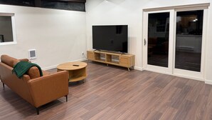 Een moderne woonkamer met een bruine leren bank, een ronde houten salontafel en een flatscreen televisie op een houten meubel.