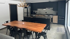 A modern kitchen with dark cabinets, a central island, stainless steel appliances, and a wooden dining table with chairs. - St-Alexis en escapade nature et spa. Accès aux pistes de motoneiges a 3 minutes. (Saint-Alexis-des-Monts)