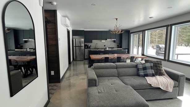 A modern kitchen with dark cabinets, a stainless steel refrigerator, and a dining area with a wooden table and chairs. - St-Alexis en escapade nature et spa. Accès aux pistes de motoneiges a 3 minutes. (Saint-Alexis-des-Monts)