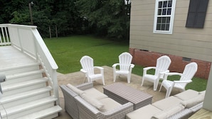 Un patio con mobiliario de mimbre, sillas Adirondack blancas y suelo de hormigón.