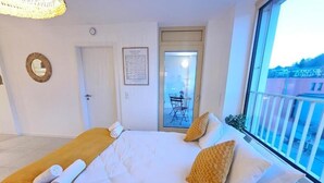 A hotel room with a bed, a window with a view, a door, and a small table with chairs outside. - New 2BR Flat in Limpertsberg City center (Luxembourg City)