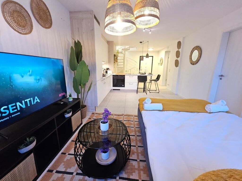 Camera d'albergo moderna con una grande TV, un letto, un'area pranzo e una cucina sullo sfondo.
