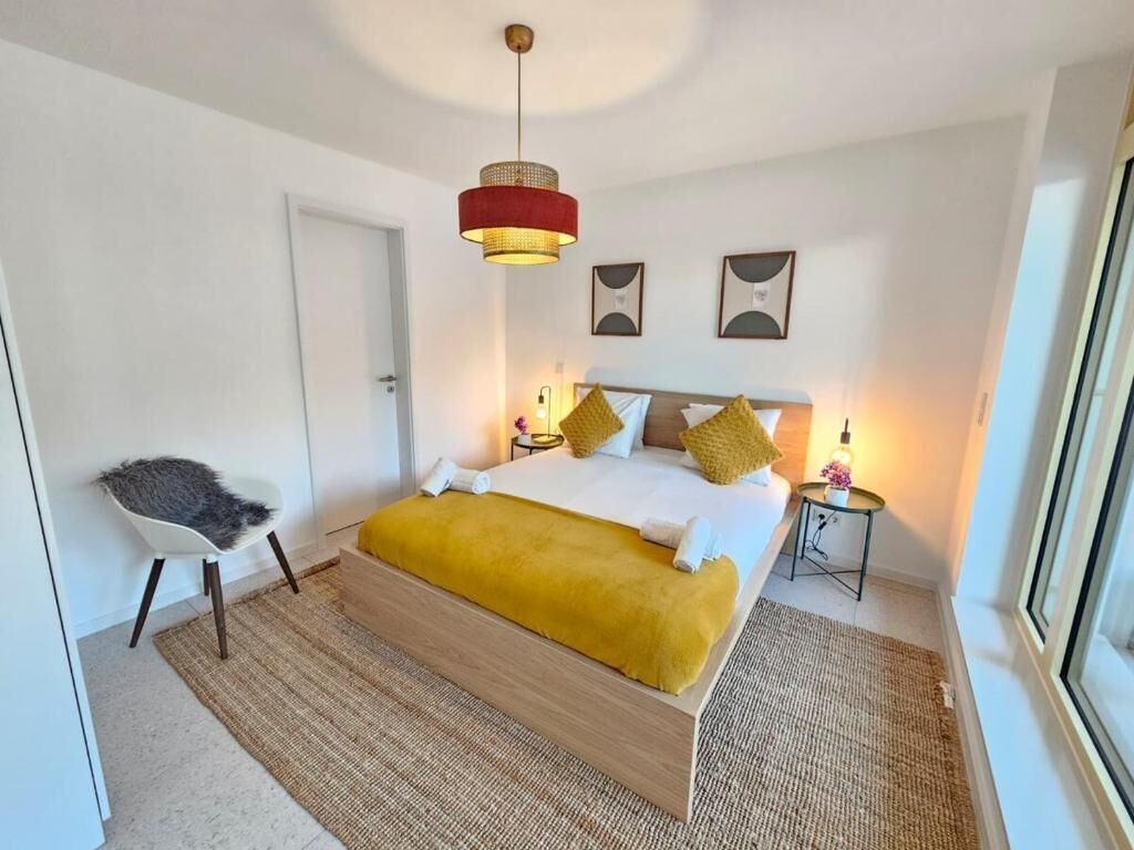 Un dormitorio moderno con una cama, una silla, una mesita de noche y una lámpara colgante.