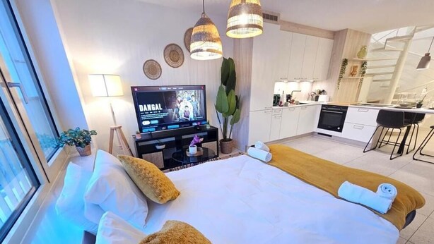 A modern hotel room with a large bed, a TV, a kitchen area, and a dining space. - New 2BR Flat in Limpertsberg City center (Luxembourg City)