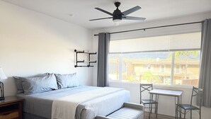 A bedroom with a bed, bedside table, and a window with a view of buildings.