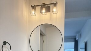 Ein modernes Badezimmer mit einem runden Spiegel, drei schwarzen Wasserhähnen und einer Holzkommode.
