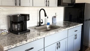 Eine moderne Küche mit grauen Schränken, einer schwarzen Mikrowelle, einer schwarzen Kaffeemaschine und einer Spüle aus Edelstahl.