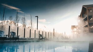 A pool with chairs and a building in the background. - The Aspen Hydeaway at Ascent (Canmore)