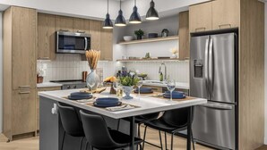 A modern kitchen with a central island, stainless steel appliances, and black pendant lighting. - The Aspen Hydeaway at Ascent (Canmore)