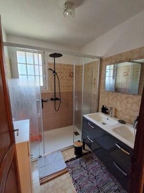 Un baño con cabina de ducha de vidrio, un lavabo con espejo y un tapete estampado.