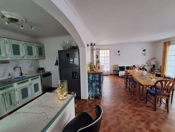 Una cocina con armarios verdes, un refrigerador negro y un comedor con sillas de madera y una mesa.