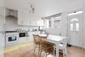 A modern kitchen with white cabinets, a stove, microwave, and a dining area with a table and chairs. - Brilliantly Located 2BDR Flat in Barbican (Greater London)