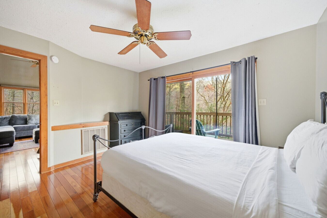 Ein Schlafzimmer mit Bett, Deckenventilator, Kommode, Schreibtisch und Blick auf Bäume durch ein Fenster.