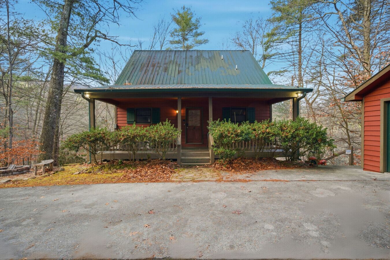 A cabin with a porch, surrounded by trees and a gravel driveway.
