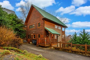A two-story log cabin with a green roof, a porch, and a fenced deck. - Smokies Mountain Charm: Views, Hot Tub, Game Room! (Sevierville)