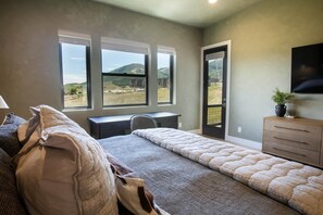 Un dormitorio con cama, escritorio y cómoda. Se observan amplios ventanales con vistas a un paisaje montañoso.