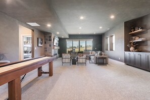 A modern living room with a pool table, comfortable seating, and a large window offering a view of the outdoors. - 4BR Deer Valley East | Hot Tub | Shuttle + Views (Wasatch County)