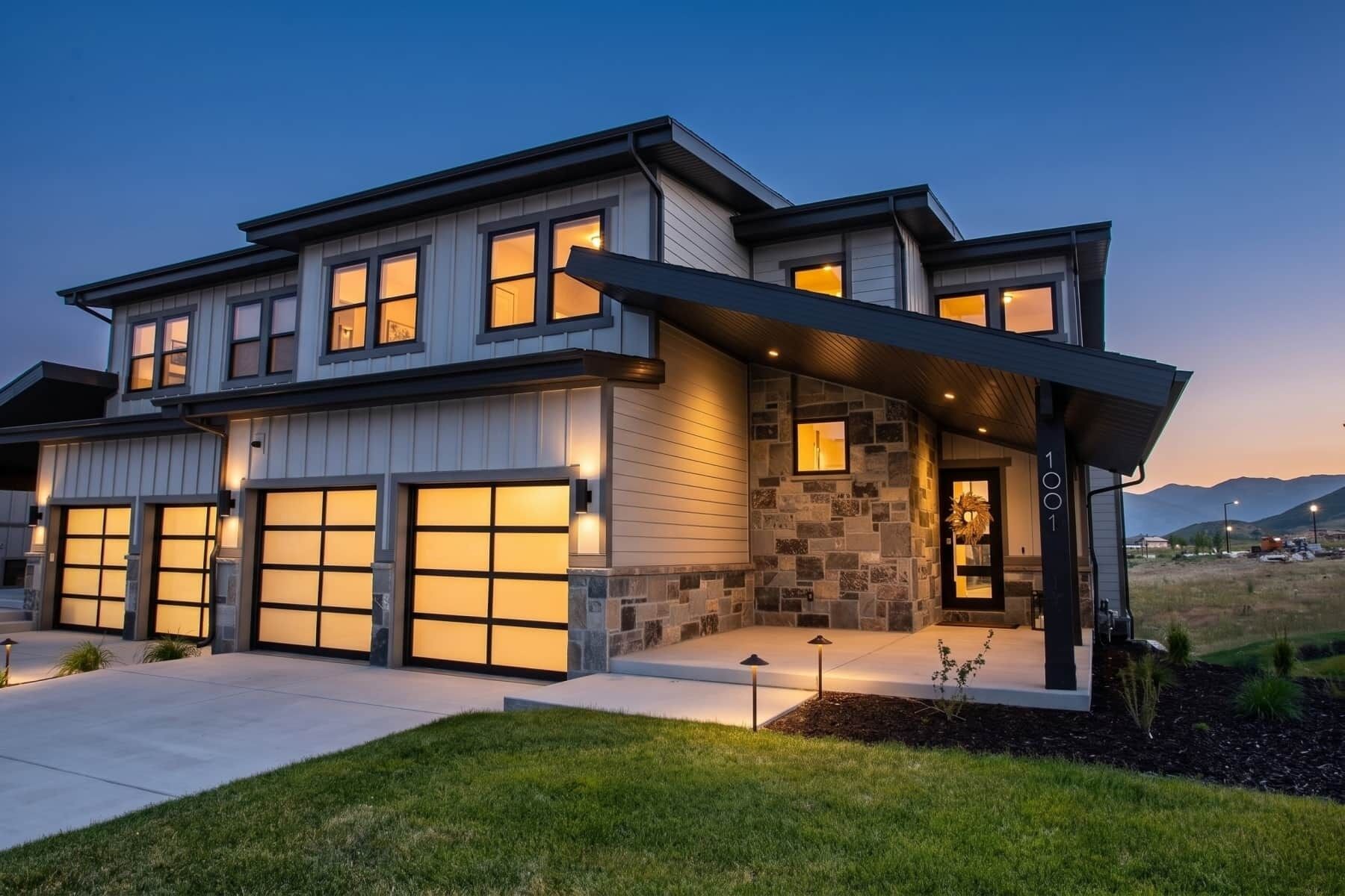 A modern two-story house with a garage, stone facade, and a well-lit entrance.