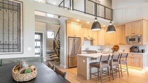 A modern kitchen with wooden cabinets, a stainless steel refrigerator, and a central island with bar stools. - 4BR Deer Valley East | Hot Tub | Shuttle + Views (Wasatch County)