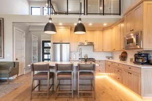 Eine moderne Küche mit Holzschränken, einem Edelstahlkühlschrank, einem eingebauten Backofen und einer Kaffeemaschine.