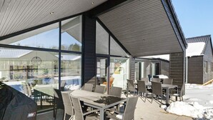 Eine Terrasse im Freien mit Tisch und Stühlen, großen Fenstern und einem mit Schnee bedeckten Boden.