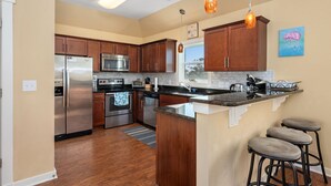 A modern kitchen with wooden cabinets, stainless steel appliances, and a bar area with stools. - 8Min Walk2Beach,Hot tub, GameRM, Family (Corolla)