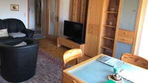 Un salon avec un canapé noir, un meuble TV en bois, une table en verre et un buffet en bois doté d’étagères.