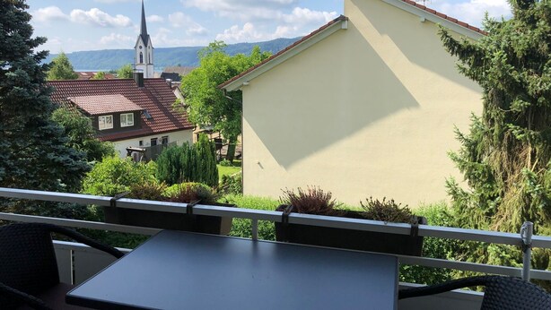 Un balcon avec une table et des chaises, d’où l’on peut admirer une église et un bâtiment avec un toit rouge.