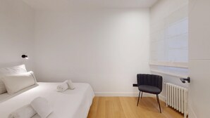 Ein schlicht eingerichtetes Schlafzimmer mit einem Bett, einem Sessel und einer Heizung.
