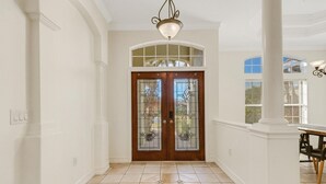 A hallway with a double door, a chandelier, and a dining area with a table and chairs. - Elegant 4-bed Home w/ Pool & Spa Near Siesta Key (Sarasota)
