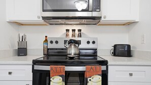 Een keuken met een fornuis, magnetron en broodrooster. Er hangen twee handdoeken aan de ovenhandgrepen, één met 'ATTE' en de andere met 'LATT'.