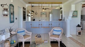 A living room with two wicker chairs, a coffee table, a ceiling fan, and a kitchen in the background. - Beachy Oasis/Solar Power/Pool/Vibe 4 all ages/Big Groups 4 Family Gatherings (Manatí)