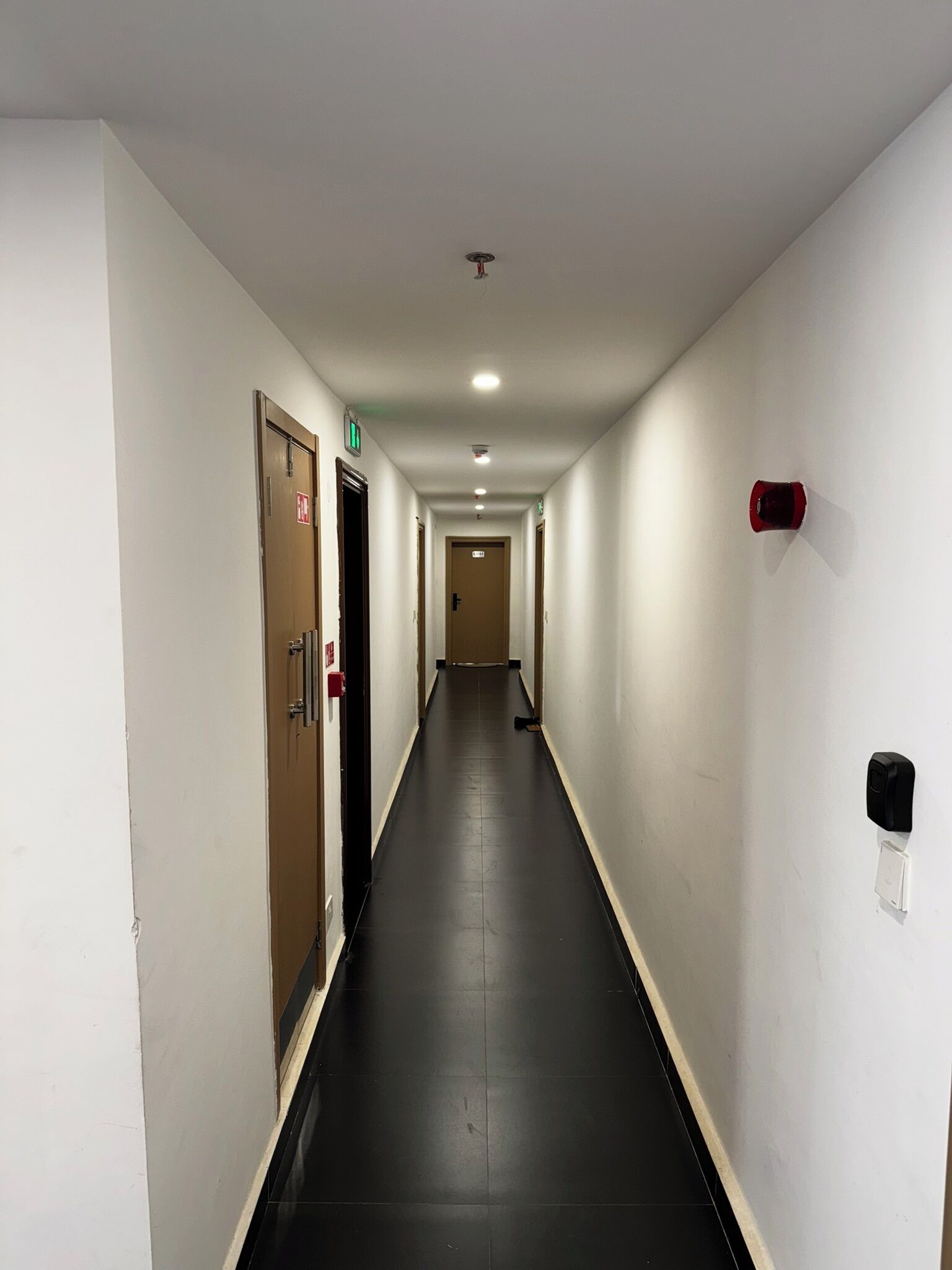 Ein langer, schmaler Hotelgang mit Türen an beiden Seiten, einem Feuermelder an der rechten Wand und einer Wandhydrantenanlage.