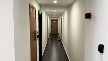 Ein langer, schmaler Hotelgang mit Türen an beiden Seiten, einem Feuermelder an der rechten Wand und einer Wandhydrantenanlage.